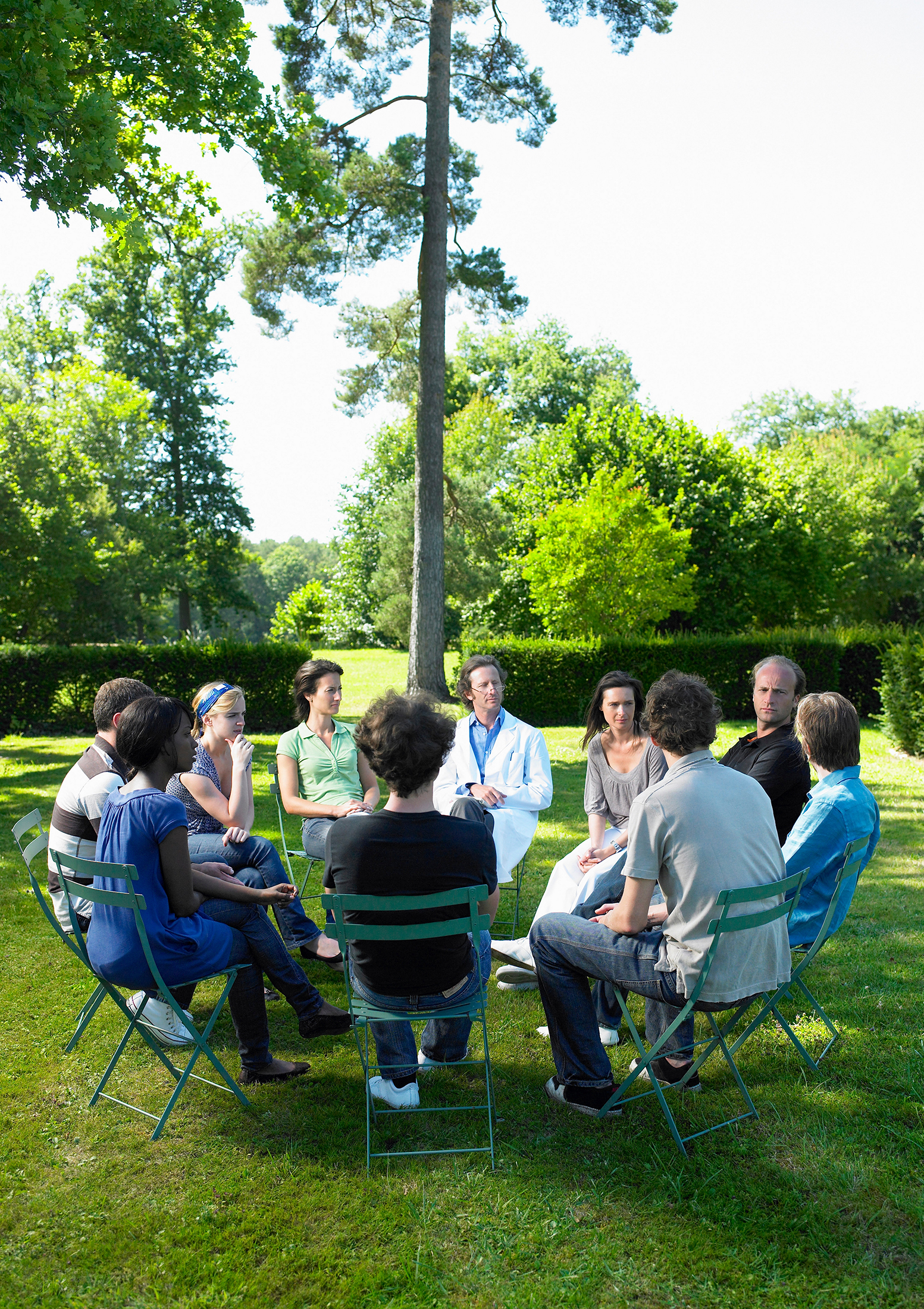 A group of people sitting in a circle, outside on the grass. Looks like an outdoor business meeting.