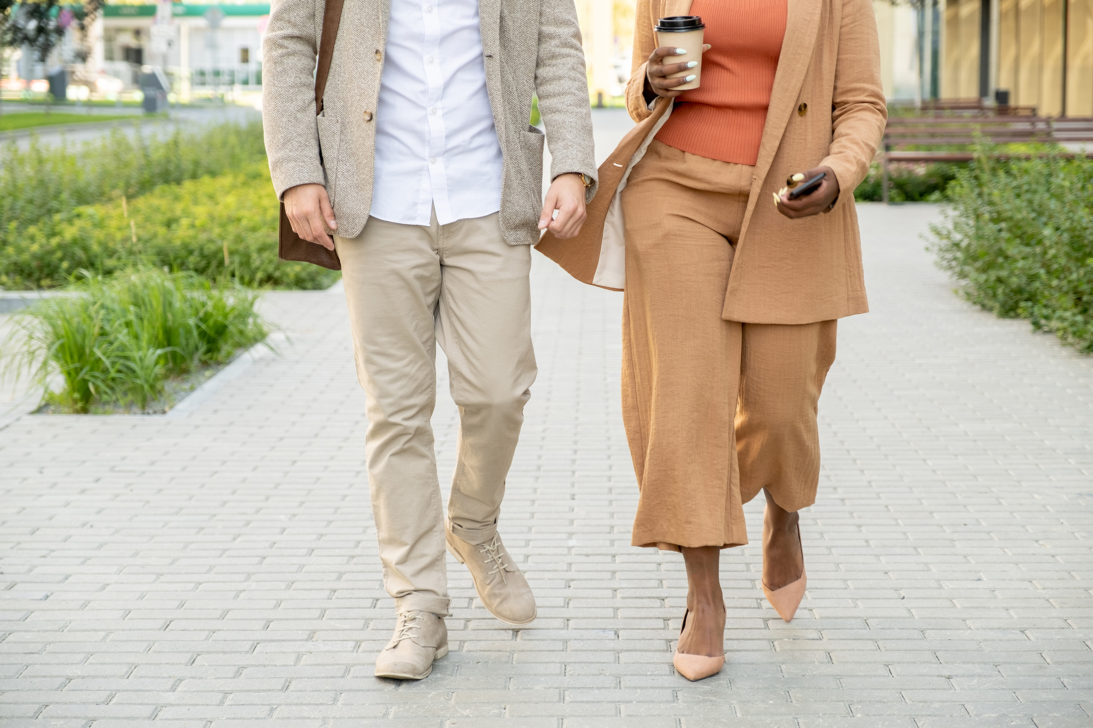 Two people walking together in business attire on a paved walkway.