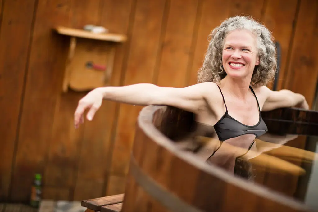 Guest smiling and relaxing in a wooden hot tub in the sauna house at Chimney Hill Estate.