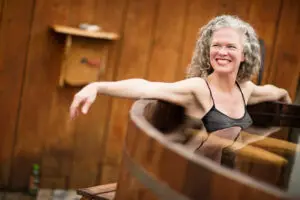 Guest smiling and relaxing in a wooden hot tub in the sauna house at Chimney Hill Estate.