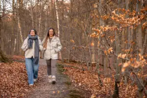 Photo of two women in heavy coats and scarves walking on a trail with leaves all around them.